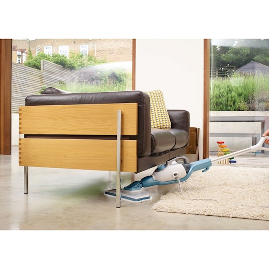 BLACKDECKER FSMH1321 steam mop cleaning under a wooden sofa, light blue and white model on indoor floor.