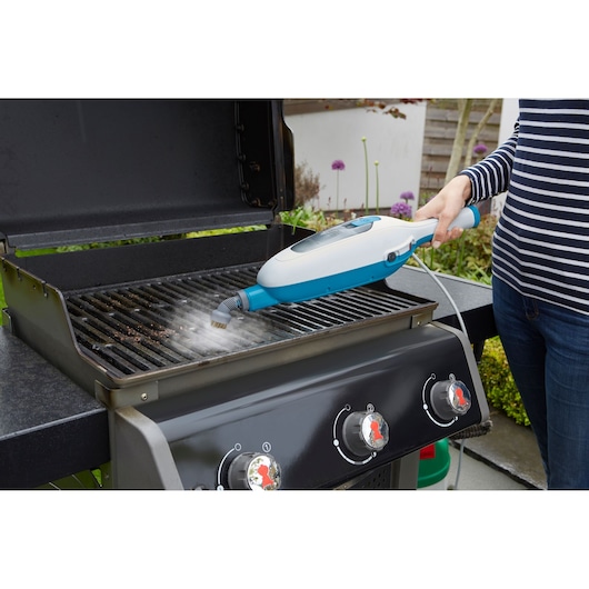 BLACKDECKER FSMH13E5 steam cleaner used to clean barbecue grill outdoors, side angle.