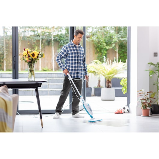 BLACKDECKER FSMH13E5 steam mop used on tile floor in modern home, with plants and soccer ball in background.