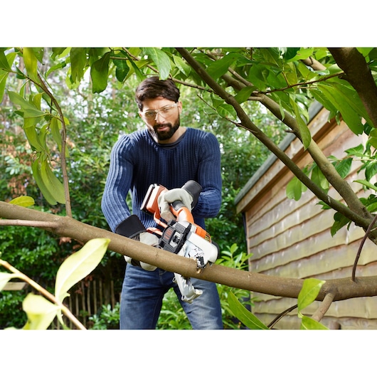 Photo of BLACKDECKER GKC1000L cordless chainsaw cutting tree branch outdoors.