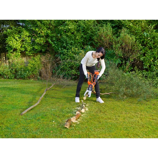 BLACKDECKER GKC1000L cordless chainsaw cutting tree branches in a garden setting.