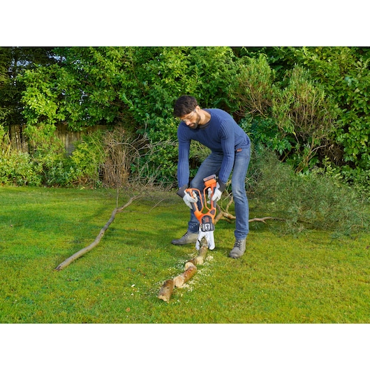 BLACKDECKER GKC1000L cordless chainsaw in use outdoors cutting a branch on grass.