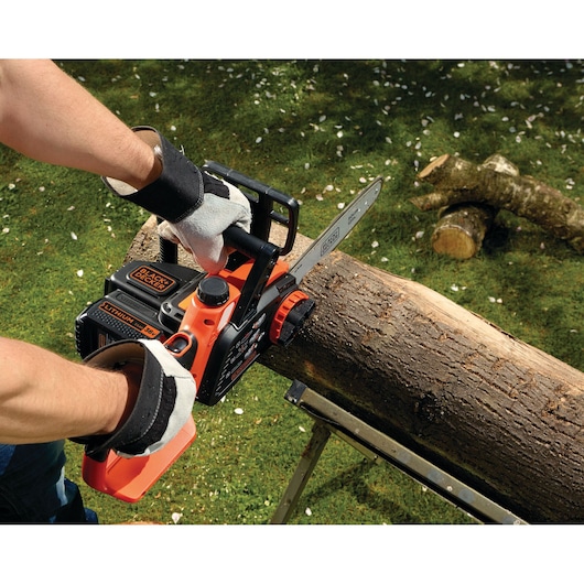 BLACK+DECKER GKC3630L25 cordless chainsaw cutting a log outdoors, user wearing gloves for safety.
