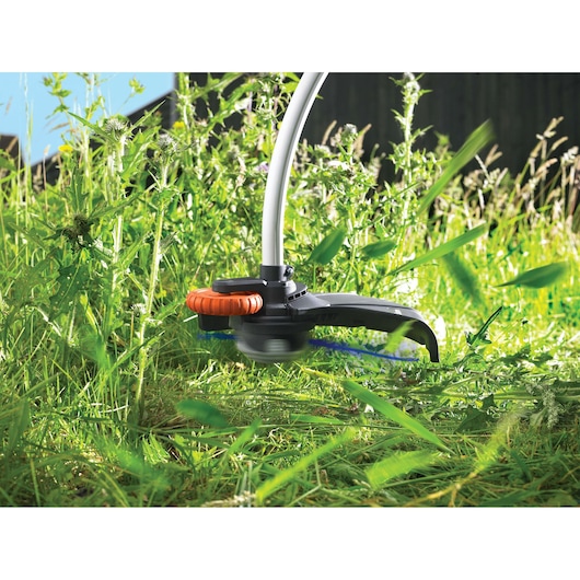 BLACKDECKER GL9035 grass trimmer in use, close-up view cutting tall green grass outdoors.