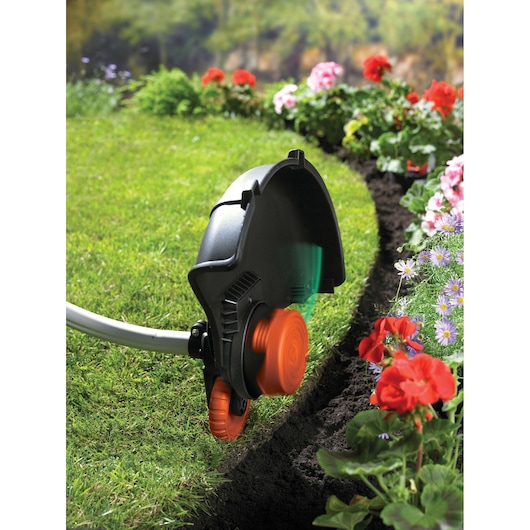BLACKDECKER GL9035 grass trimmer edging a lawn beside colorful flowers in a garden, close-up outdoor view.