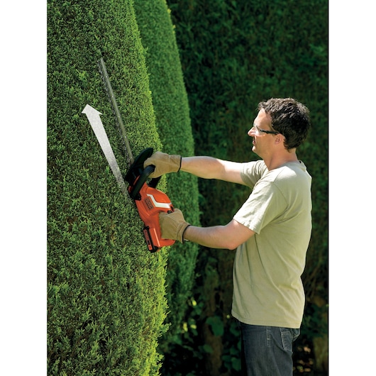 Photo of a person using BLACK+DECKER GTC1845L20 cordless hedge trimmer on a green hedge outdoors.