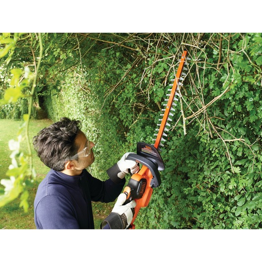 BLACKDECKER GTC18502PC hedge trimmer in use trimming green bushes outdoors.