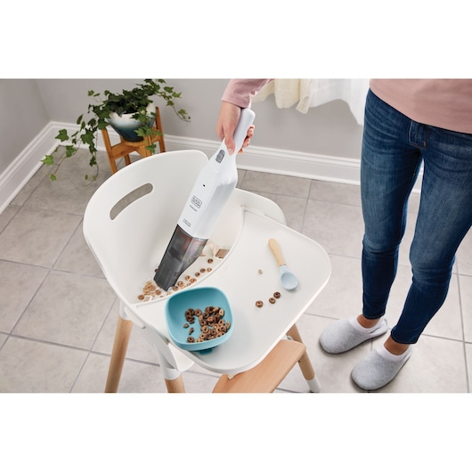 BLACKDECKER HLVC315J11 handheld vacuum cleaning spilled cereal on high chair tray, indoor setting.