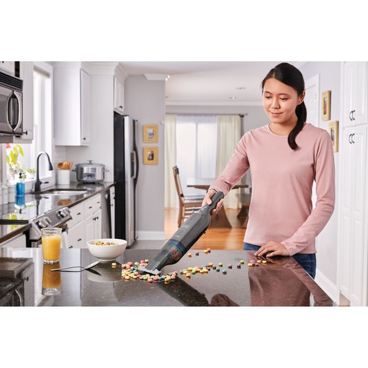 BLACKDECKER HLVC320B11 handheld vacuum cleaning spilled cereal on kitchen counter, person using in home setting.