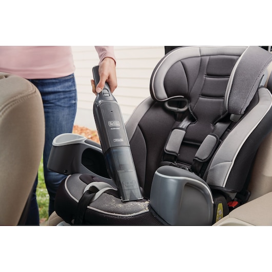 Photo of BLACK+DECKER HLVC320J11 handheld vacuum cleaning crumbs from a child's car seat.