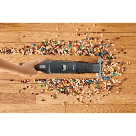 Photo of BLACK+DECKER HLVC320J11 hand vacuum cleaning mixed nuts and candy on wooden floor.