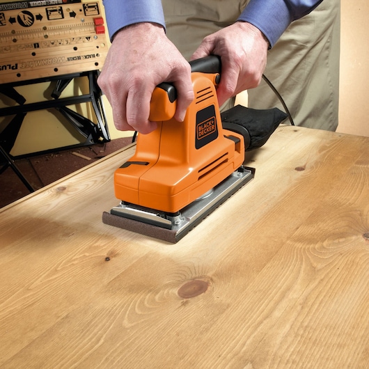 Photo of BLACK+DECKER KA274EKA orange sheet sander being used on a wooden surface.