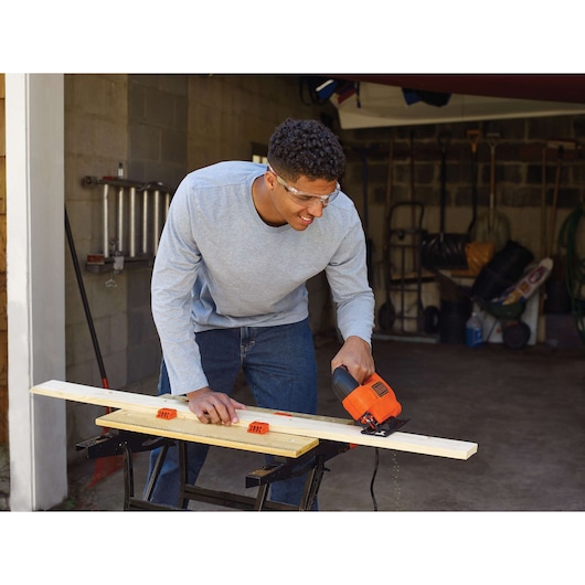 BLACKDECKER KS701E jigsaw used to cut wood plank in workshop setting, product photography.