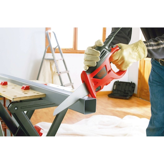 BLACKDECKER KS880EC electric saw cutting metal pipe, person wearing gloves, indoor workshop setting.