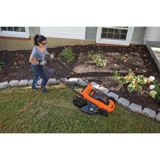 Photo of a person using a BLACK+DECKER LM2000 electric lawn mower on grass beside a flower bed.