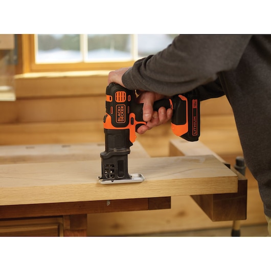 BLACKDECKER MTJS1 cordless jigsaw in use cutting wood, close-up in workshop setting.
