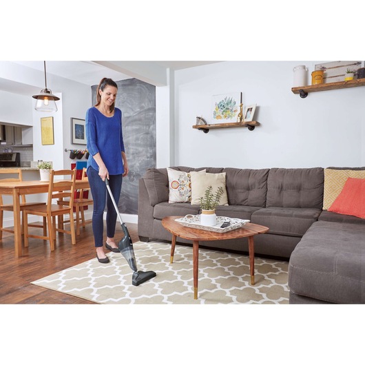 BLACKDECKER NSVA315J stick vacuum cleaning a beige patterned rug in a living room.