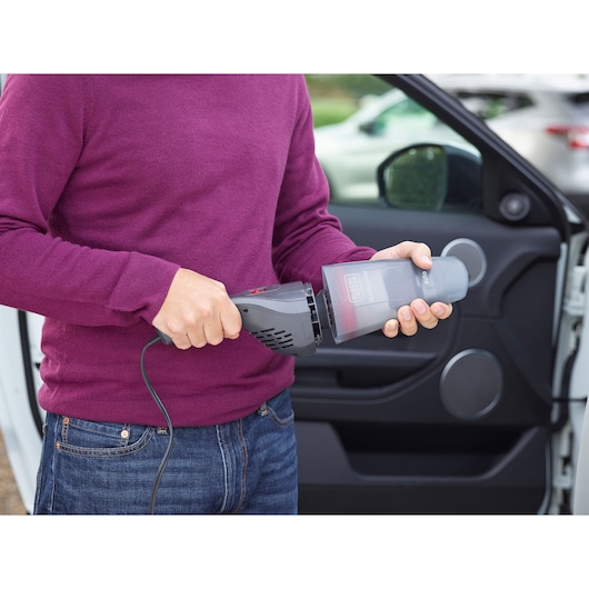 BLACKDECKER NVB12AVA handheld vacuum cleaner with dust container, shown during car cleaning.