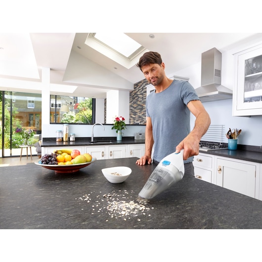 BLACKDECKER NVC115JL handheld vacuum cleaning kitchen counter with spilled oats, fruit bowl nearby.