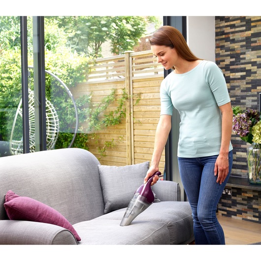 BLACK+DECKER NVC115W handheld vacuum cleaner being used on a grey sofa in a modern living room.