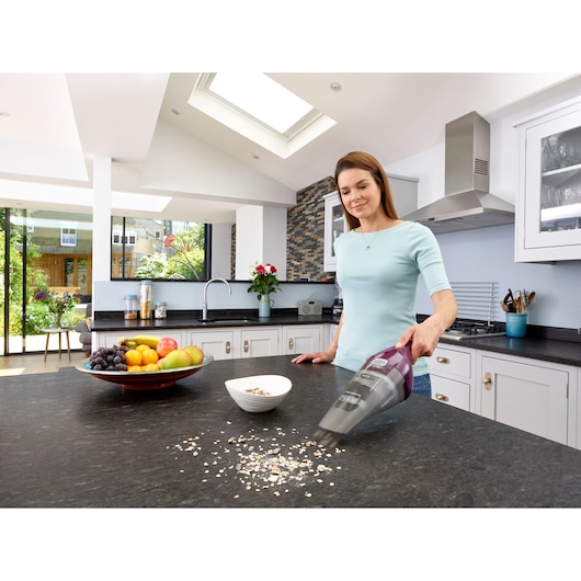 BLACKDECKER NVC115W handheld vacuum cleaning kitchen countertop with food spills, modern kitchen setting.