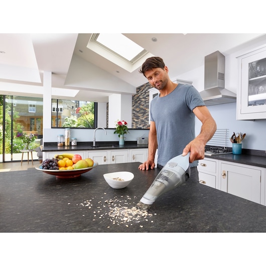 BLACKDECKER NVC215W handheld vacuum cleaning kitchen counter with spilled oats near fruit bowl.