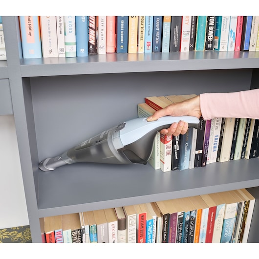 BLACKDECKER NVC215W handheld vacuum cleaning grey bookshelf near books, close-up side angle.