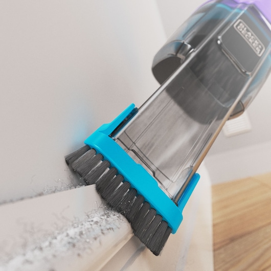 BLACKDECKER NVD220BP handheld vacuum with blue brush attachment cleaning dust from white surface, close-up angle.