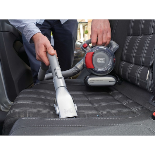 BLACKDECKER PD1200AV handheld vacuum cleaning a car seat, close-up of nozzle and flexible hose.