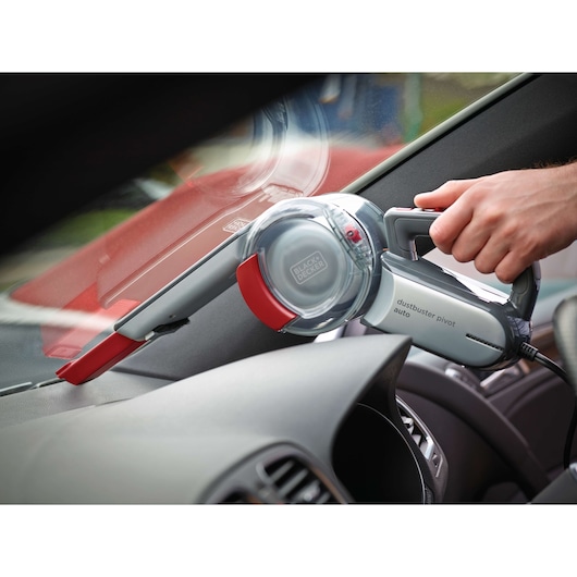 A person uses a BLACK+DECKER Dustbuster Pivot Auto handheld vacuum cleaner to clean the dashboard area inside a car.