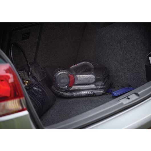 A BLACK+DECKER PV1200AV portable car vacuum cleaner stored in the trunk of a vehicle, next to a black handbag and a blue item.