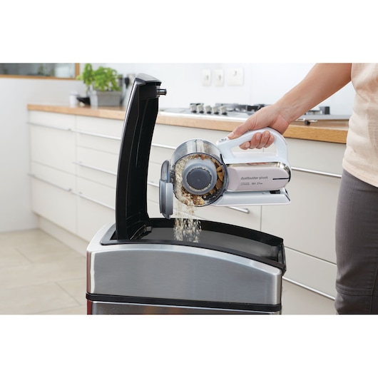 BLACKDECKER PV1820LRGP handheld vacuum being emptied into a steel trash bin in a kitchen.