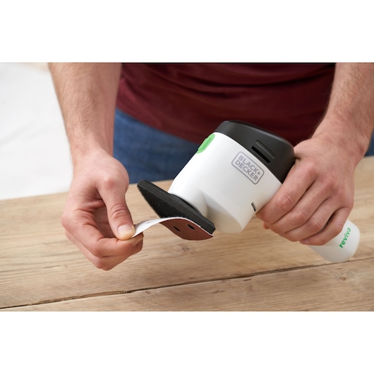 Photo of BLACK+DECKER REVDS12C sander being fitted with sanding sheet, handheld near wooden surface.