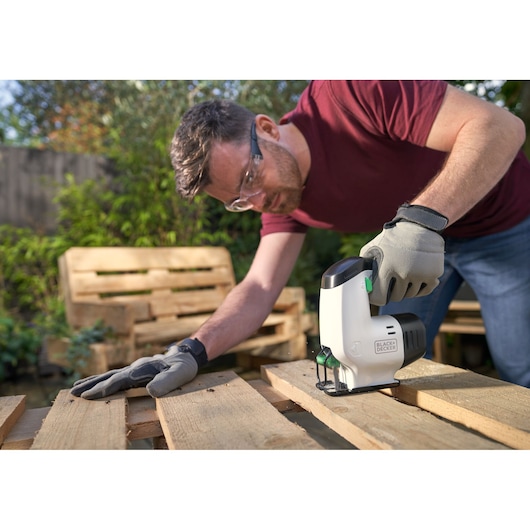 BLACKDECKER REVJ12C jigsaw used on wooden pallet outdoors by person wearing gloves.