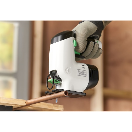 Photo of BLACK+DECKER REVJ12C jigsaw cutting copper pipe, white and black casing, gloved hand holding tool.