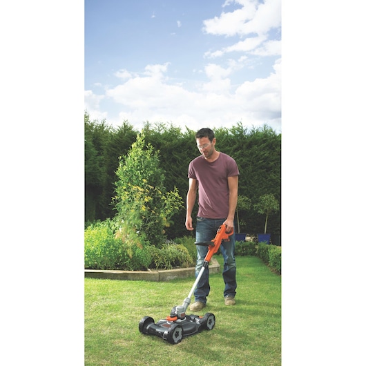 BLACK+DECKER STC1820CM lawn mower used outdoors on grass, orange and black, showing garden background.