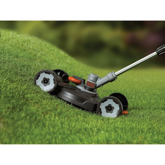 BLACKDECKER STC1820CM cordless lawn mower with grey wheels cutting grass on a slope.