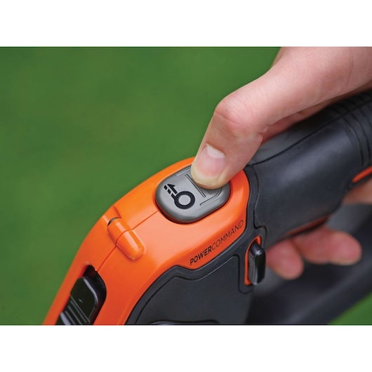 BLACKDECKER STC1820EPC close-up of Powercommand button on orange and black grass trimmer in use.