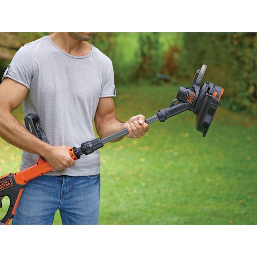 BLACKDECKER STC1820EPC orange-black cordless grass trimmer held outdoors by a person.