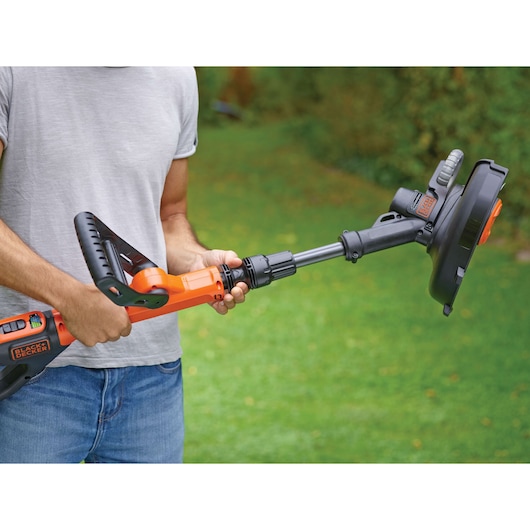 BLACKDECKER STC1820EPC orange cordless grass trimmer held outdoors, close-up of handle and shaft.