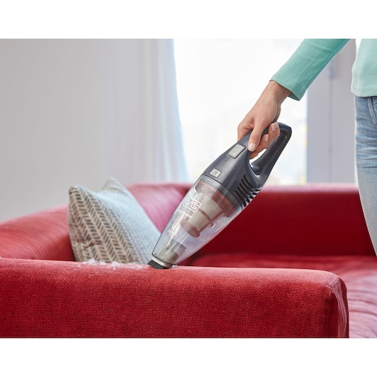 BLACK+DECKER SVB520JW handheld vacuum being used on a red sofa with patterned pillow in a bright room.