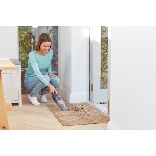 BLACKDECKER SVB620JW handheld vacuum cleaning debris on a woven mat near a glass door in a modern home.