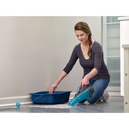 Photo of BLACKDECKER WDA320J handheld vacuum cleaning scattered litter near a blue cat tray on tiled floor.