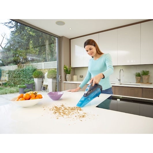 BLACKDECKER WDA320J handheld vacuum cleaning crumbs on a kitchen counter near fruit bowl.