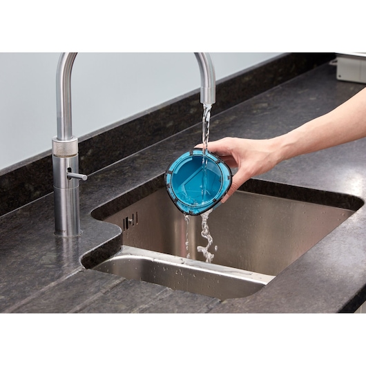 BLACKDECKER WDC215WA vacuum filter being rinsed under water in a kitchen sink.