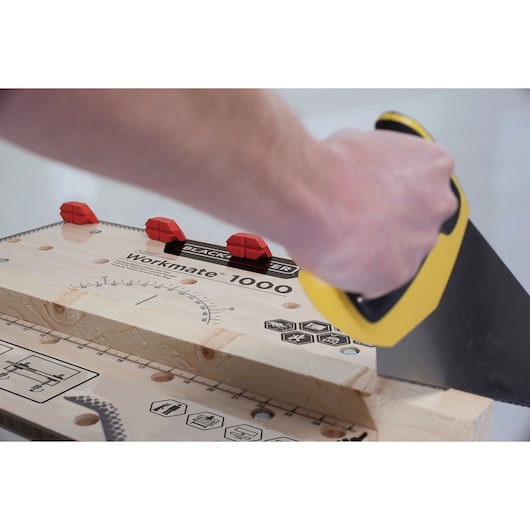 Photo of a BLACKDECKER WM1000 workbench with wood clamped and a hand using a yellow saw, close-up angle.